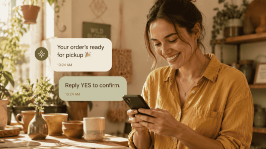 A shop owner smiles at a friendly business text on her phone in a cozy studio.